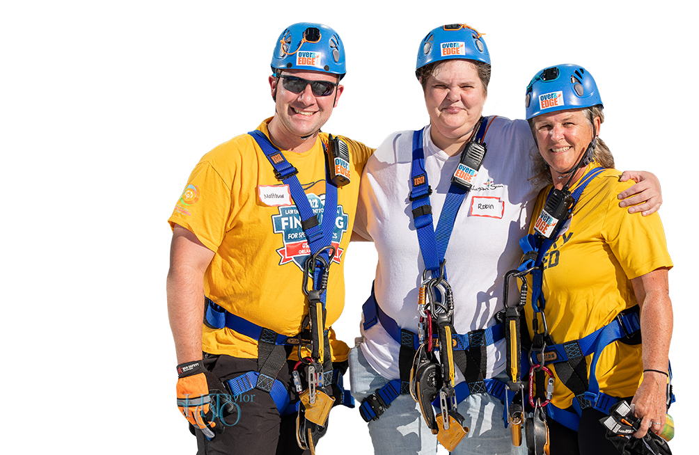 A group of smiling Over the Edge participants wearing helmets and harnesses